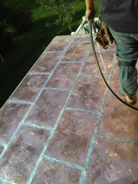 Person applying blue grout to a brown-tiled outdoor surface with a hose nearby