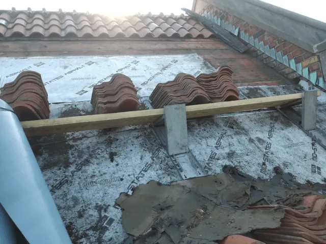 Roof under repair with wooden support beam, clay tiles, and patchy cement on a sloped rooftop.