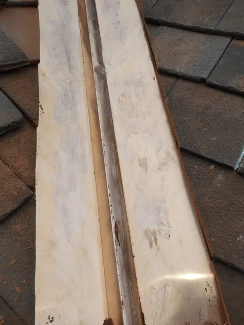 Close-up of two light wood trim pieces on a tiled floor, one with a narrow groove and worn edges