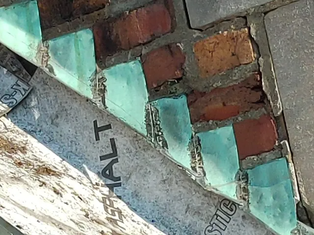 Close-up of a brick wall with turquoise paint, gray metal, and a diagonal painted sign fragment.