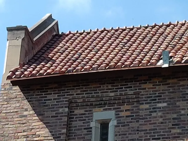 Brick house roof with red tiles and a chimney against the sky