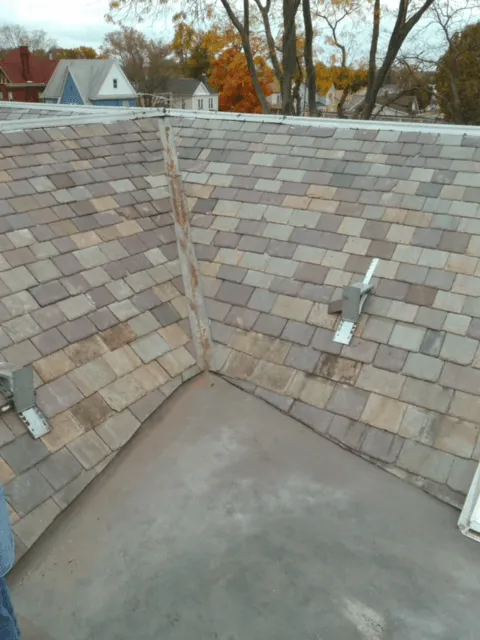 Roof valley with gray shingles and a flat section, seen from above with autumn trees in the background