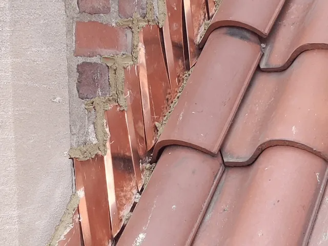 Close-up of red roof tiles beside a weathered brick wall and pale stucco surface.