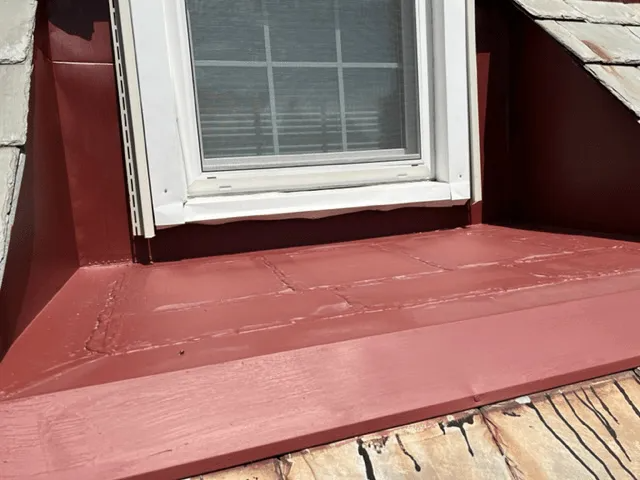 Red-painted exterior window ledge beneath a white-framed window with trim and siding