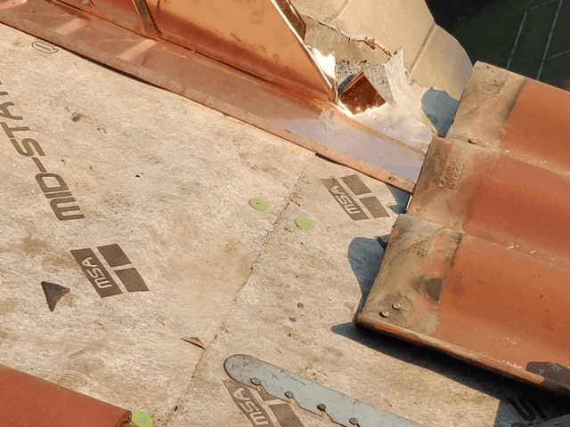 Damaged roofing with torn underlayment and broken terracotta tiles on a sloped roof