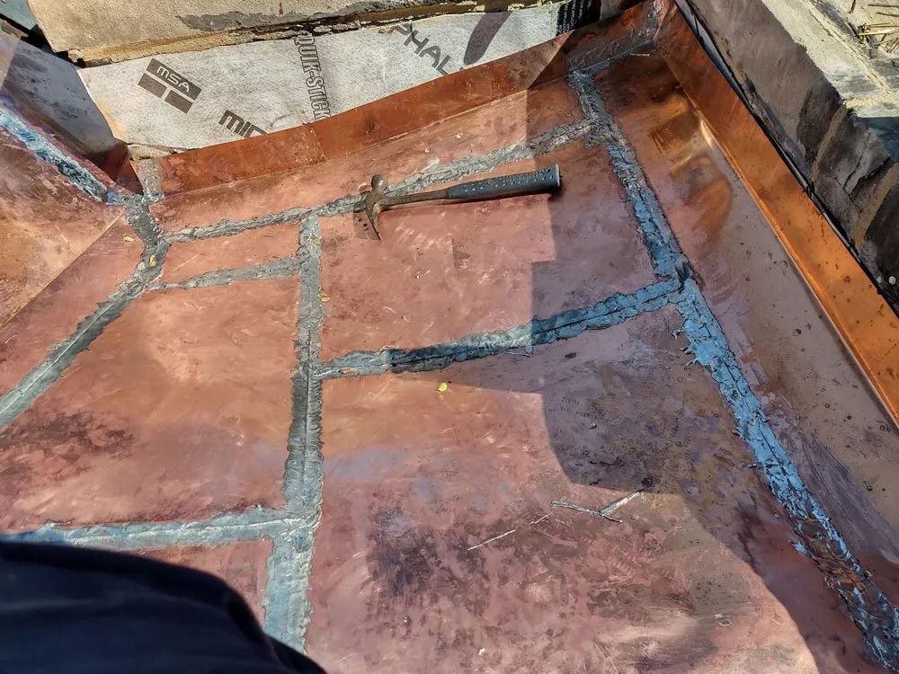 Close-up of a tiled outdoor floor with blue mortar lines and some paper scraps near the edge.