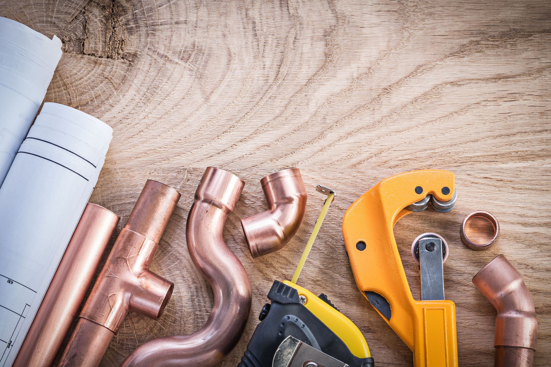 Copper plumbing pipes and fittings with blueprints and pipe cutter on wood.