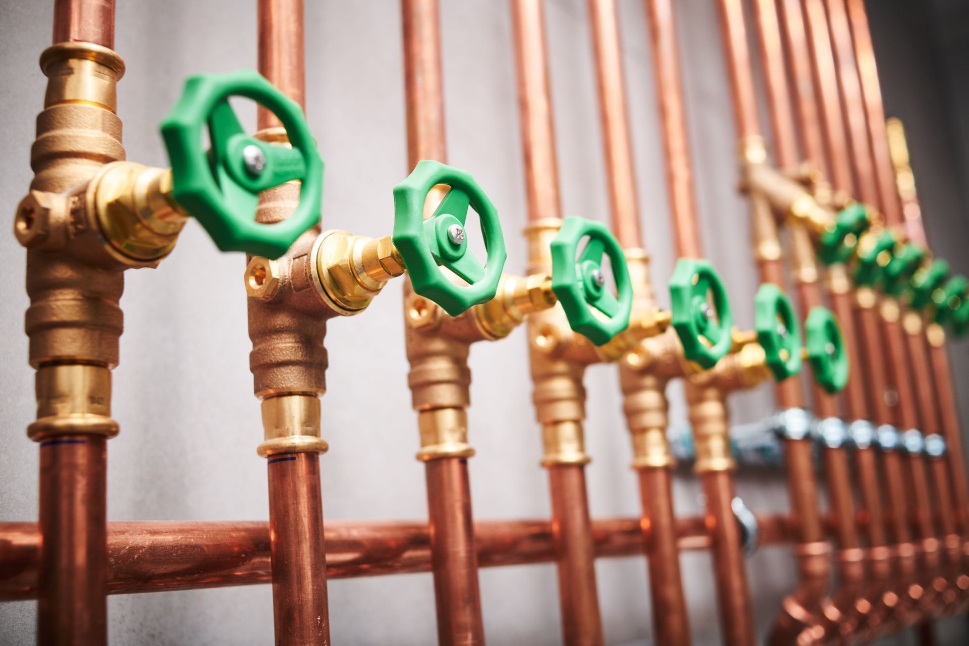 Copper pipes with brass fittings and green valves against a gray wall.