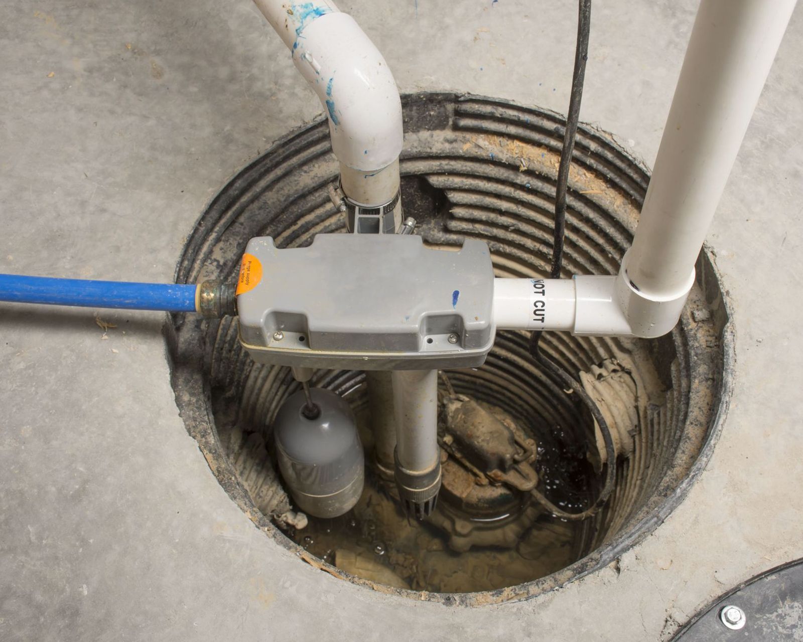 Open sump pit with pipes, pump, and wiring in a concrete floor.