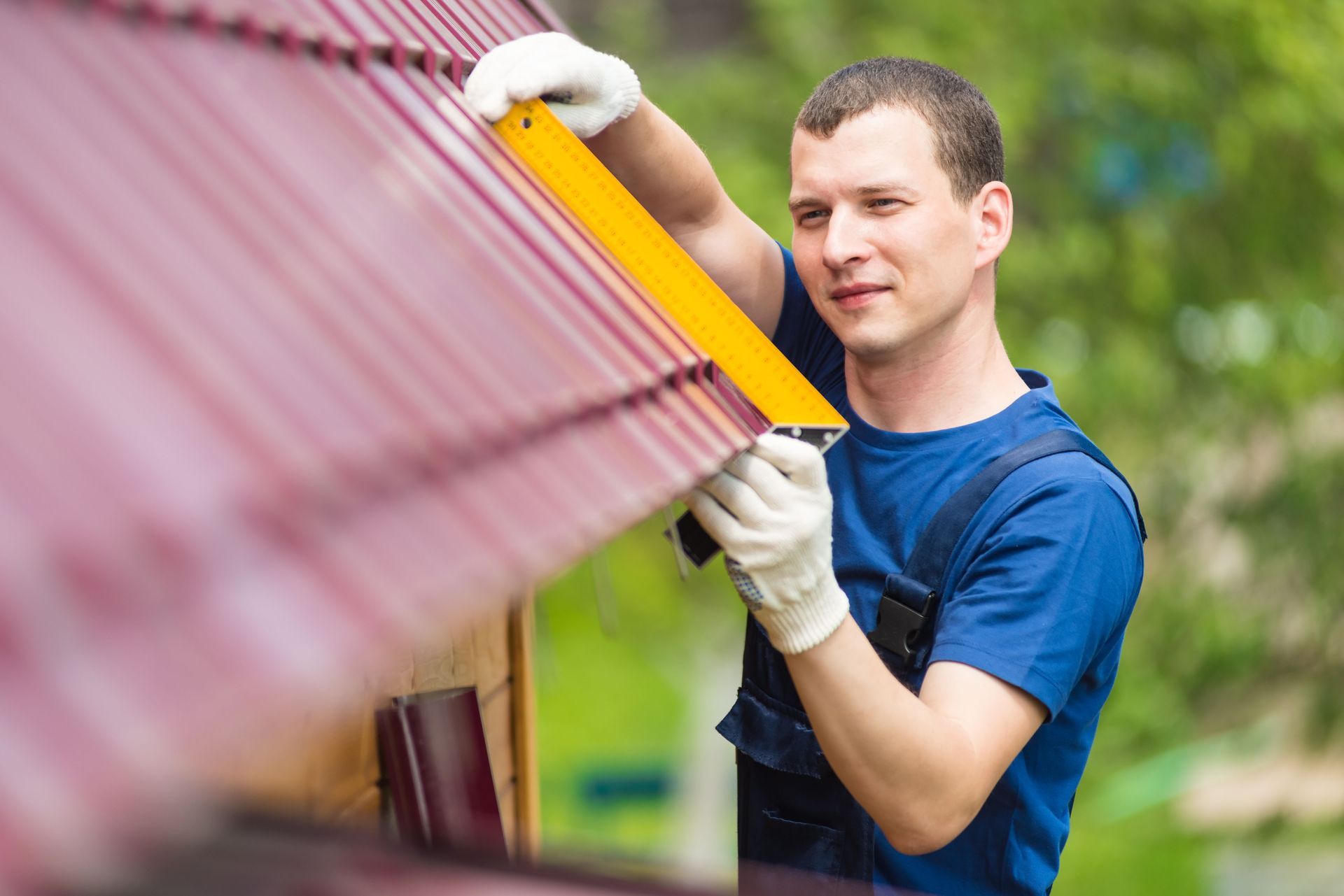 Roofer in blue shirt installing a red metal roof, using a level.