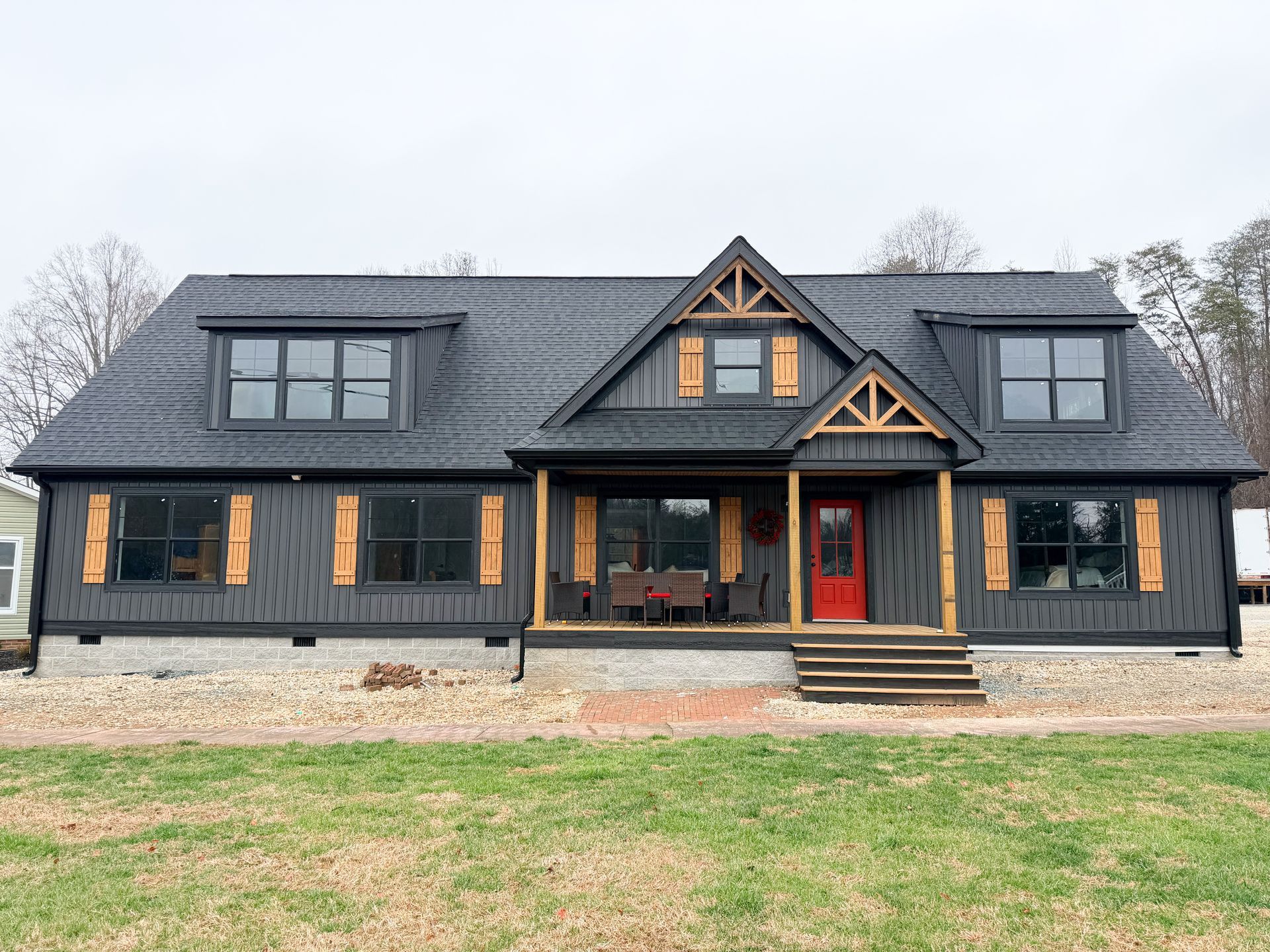 White farmhouse with black roof, turquoise door, and expansive windows.