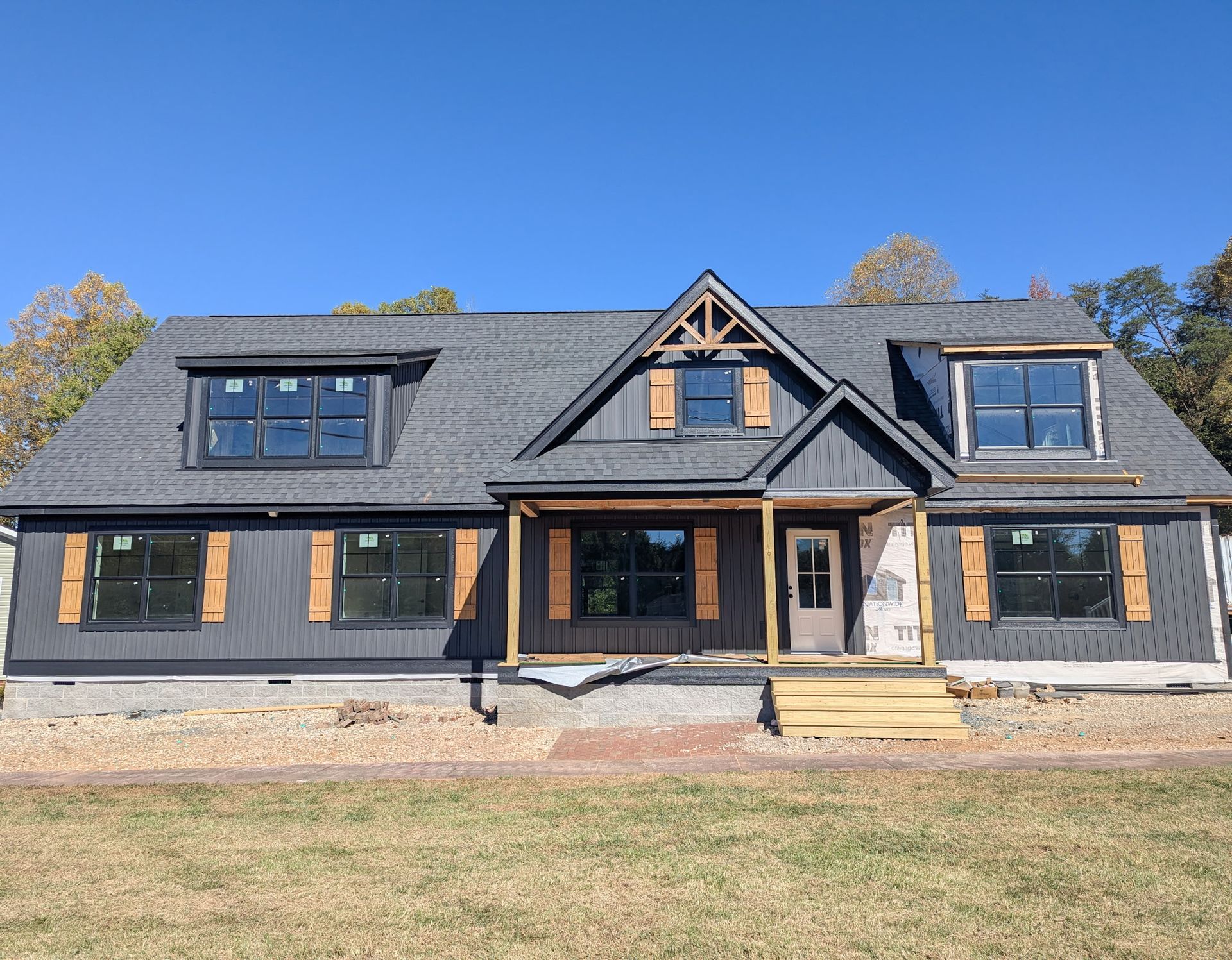 New construction house with gray siding, shutters, and dormers under a blue sky.