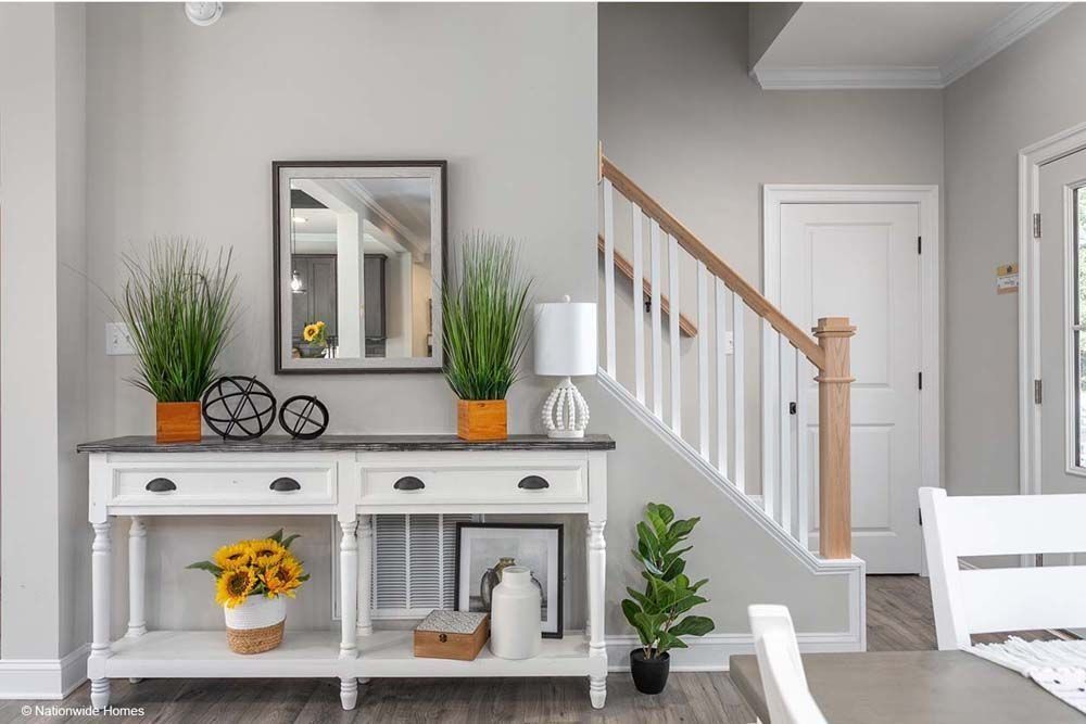 A console table with decor, including plants, a mirror, and a staircase in a light-filled entryway.