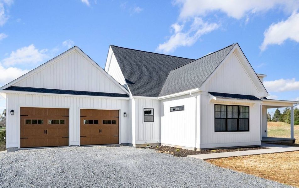White farmhouse with brown garage doors and a gravel driveway.
