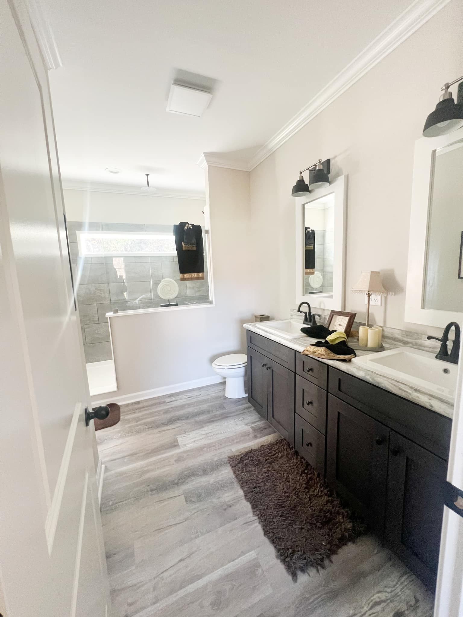 Bathroom with double vanity, dark cabinets, light gray floors, and a shower.