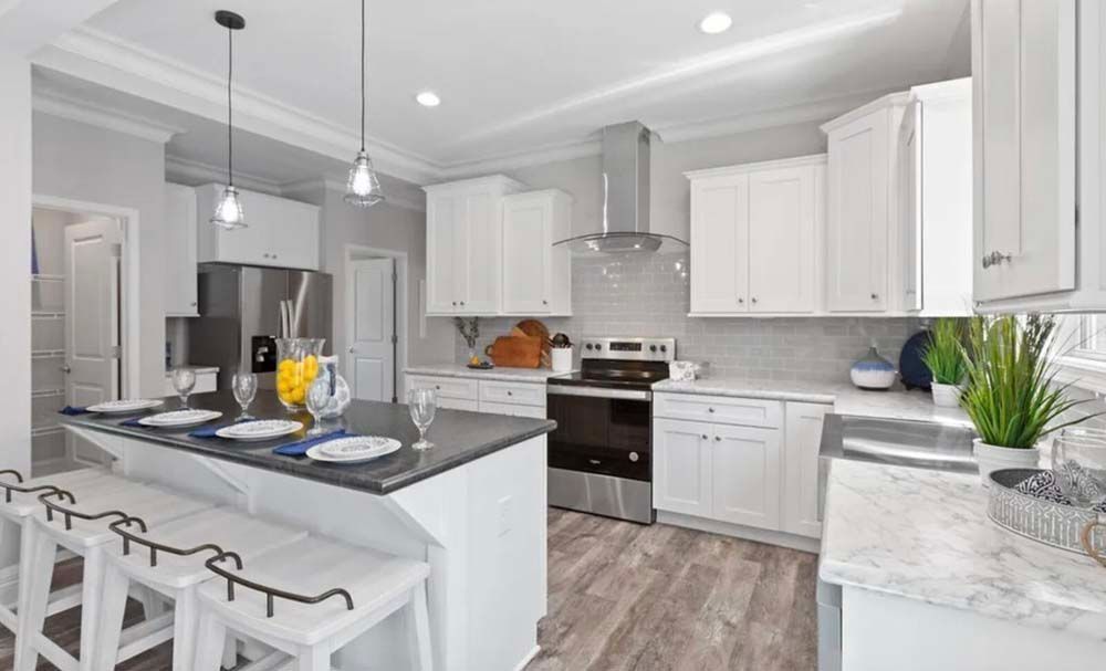 Modern white kitchen with island, stools, stainless steel appliances, and gray countertops.