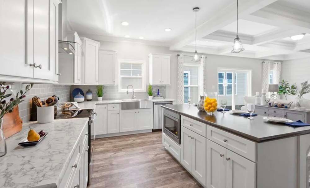 Bright white kitchen with island, cabinets, and countertop, open to a living room with light wood floors.