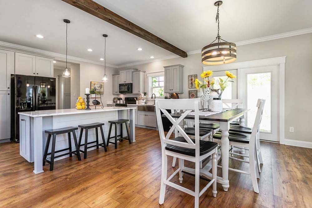 Open-concept kitchen with white cabinets, island, and dining table with a wooden floor.