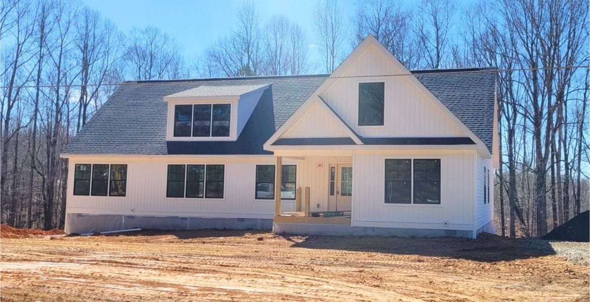 White farmhouse under construction, with windows and a small porch. Set against bare trees and blue sky.