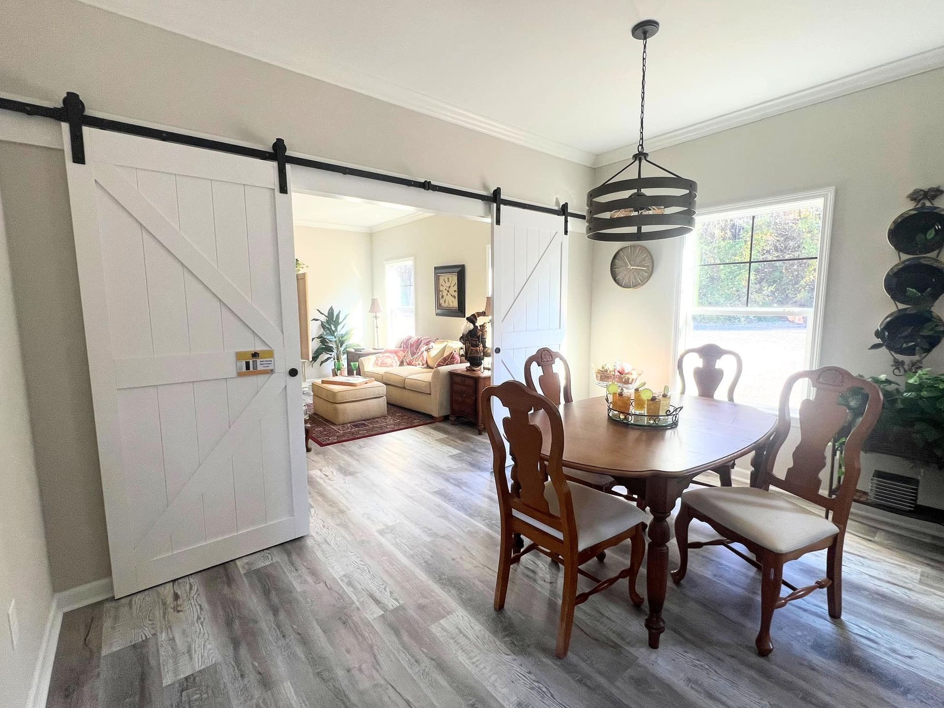 Dining room with wood table and chairs, leading to living room with barn doors.