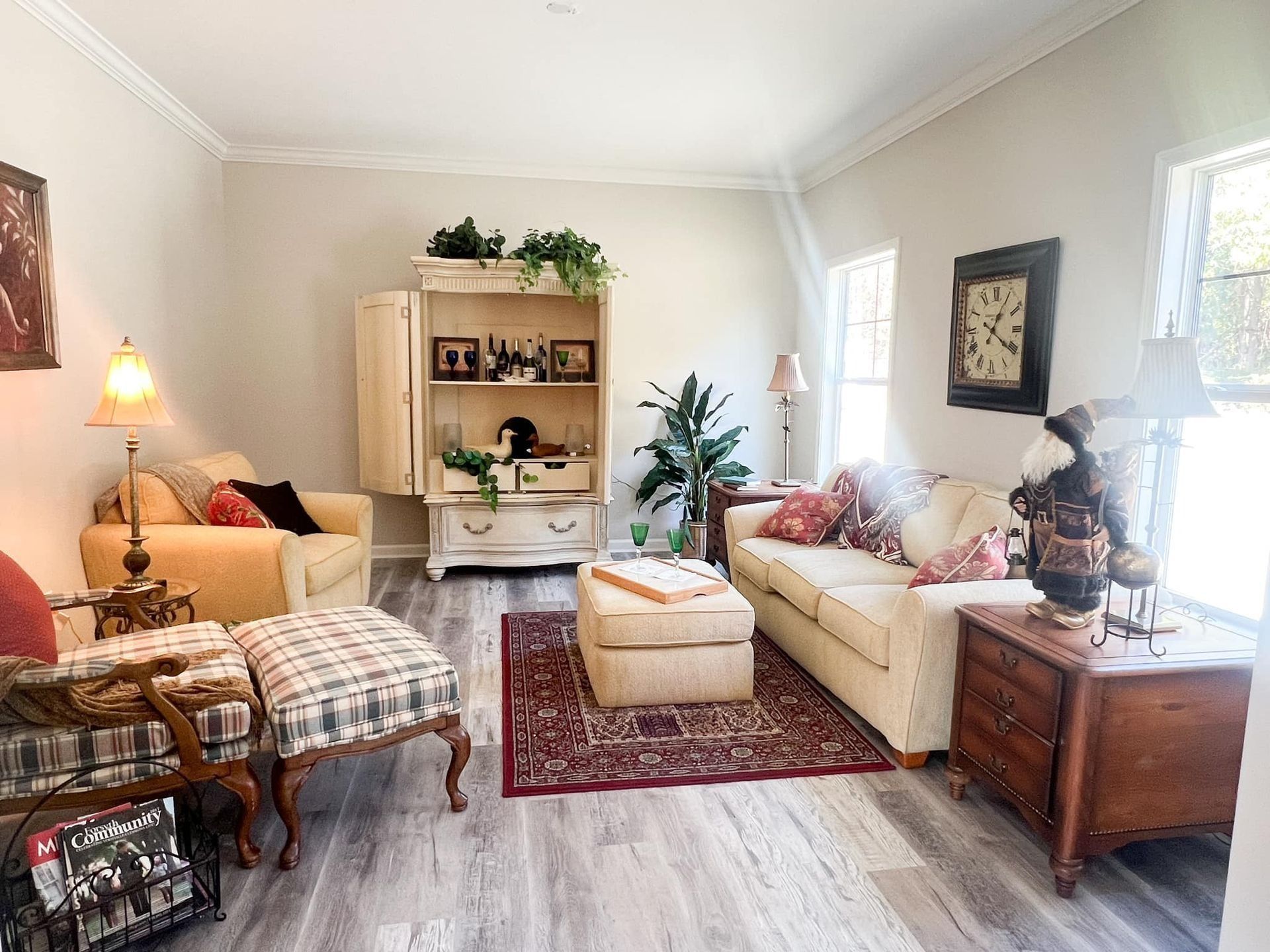 Cozy living room with cream-colored furniture, a patterned rug, and a wooden cabinet against a light-colored wall.