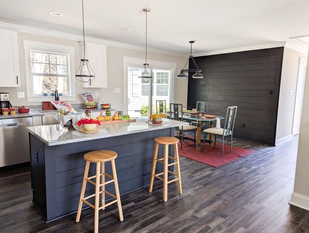 Kitchen with island and stools, dark wood floor, and dining area with black accent wall.