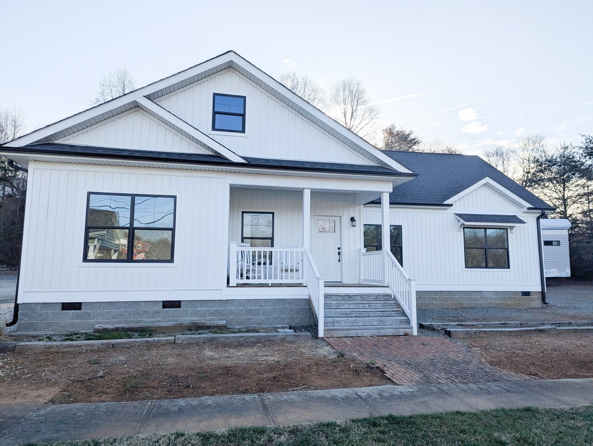 White house with black trim, porch, and dark roof, under a light sky.