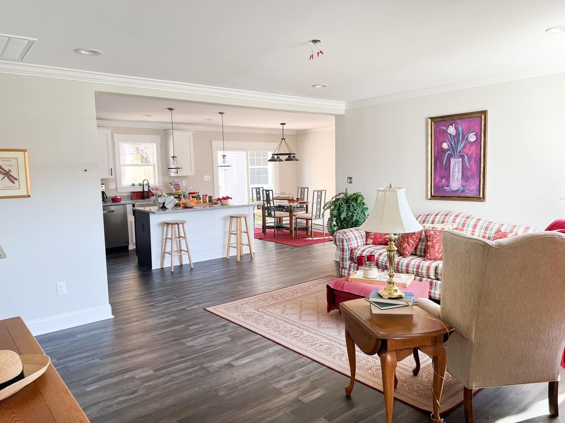 Open-concept living space: kitchen, dining, and living room areas. Gray floors, white walls, and floral furniture.