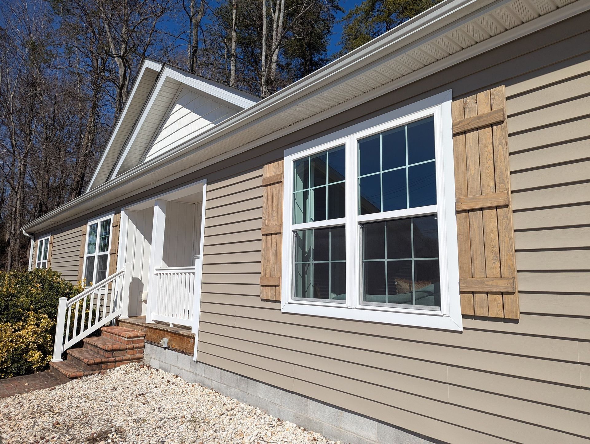 Tan house with white trim, wooden shutters, and a blue sky.