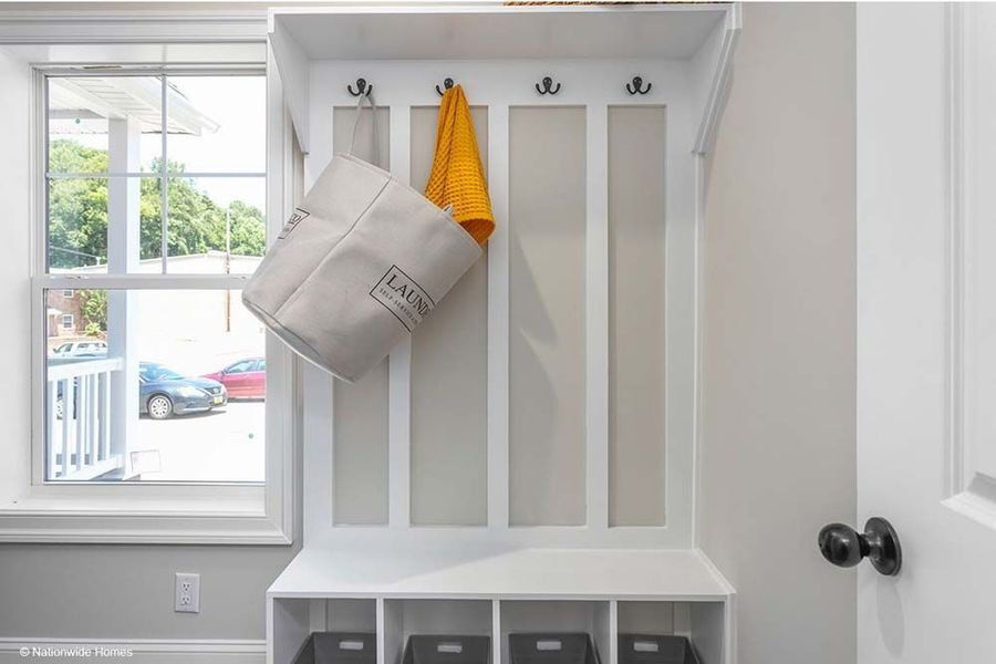 White entryway with hooks, storage, a window, and a hanging laundry basket.