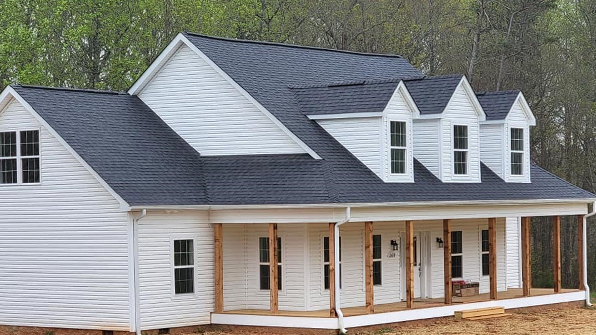 White house with a black roof, a porch, and three dormers.