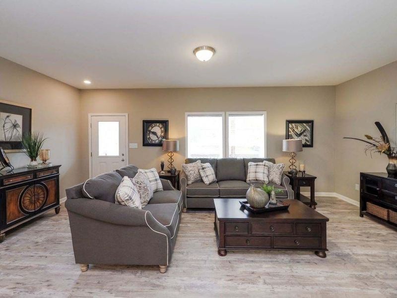 Living room with gray couches, wood furniture, beige walls, and a large window.