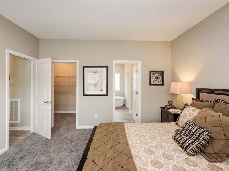 Bedroom with bed, nightstand, closet, and doorways. Soft neutral colors, carpet.
