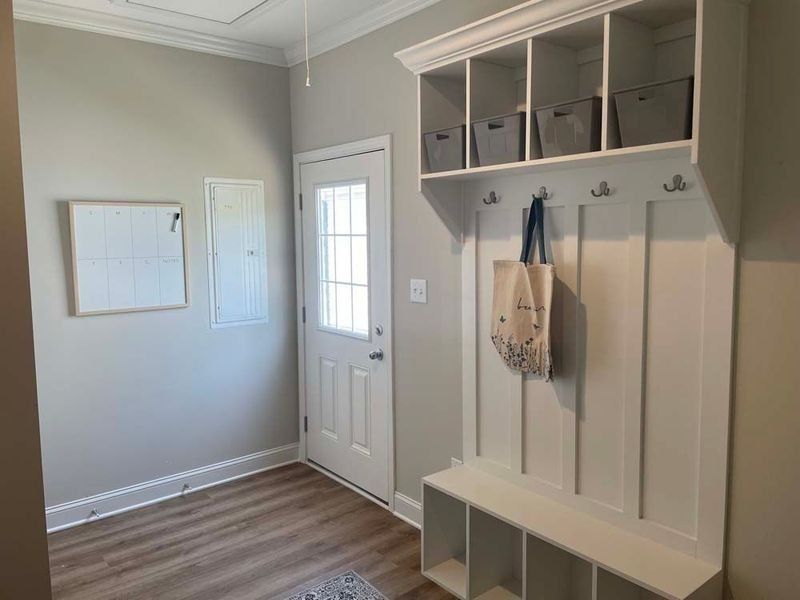 Mudroom with white door, built-in storage, and gray walls, bench, and hooks. A bag hangs from one hook.