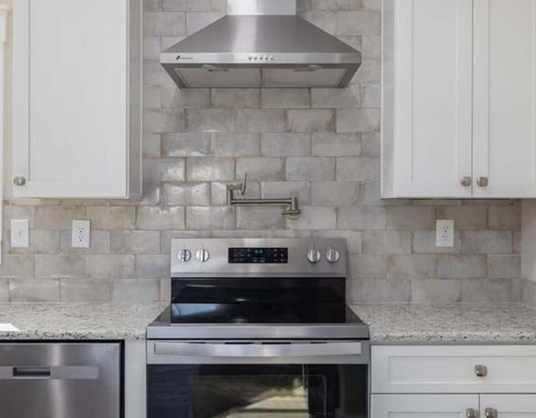 Kitchen with stainless steel appliances, white cabinets, gray backsplash, and a stove.