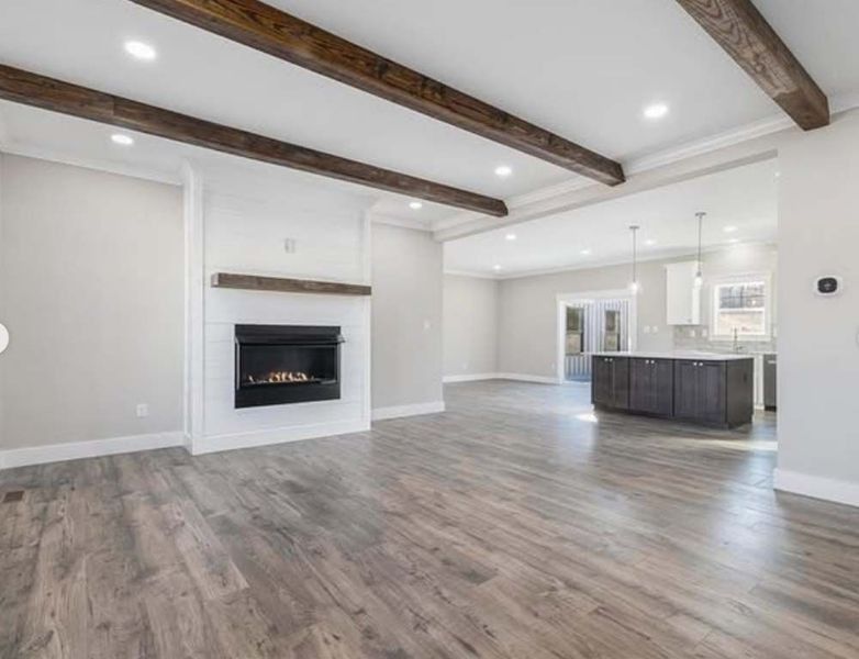 Spacious, open-concept living area with wood beams, fireplace, dark cabinets, and light wood floors.