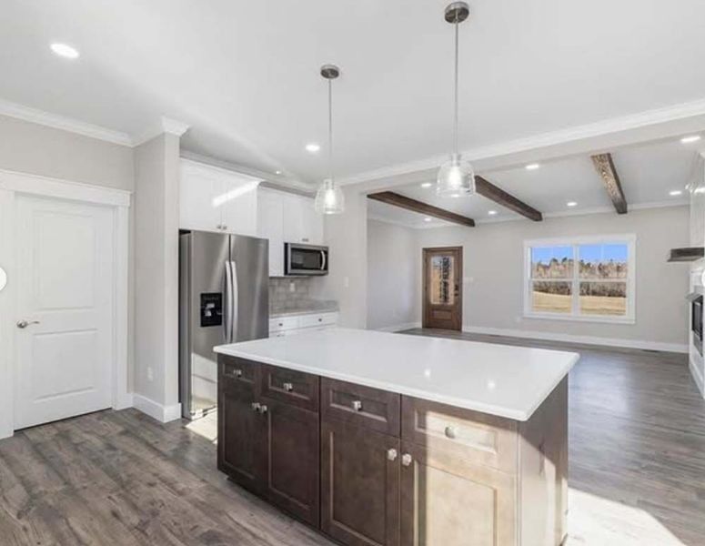 Kitchen with dark brown island, stainless steel appliances, white cabinets, and wood beams.