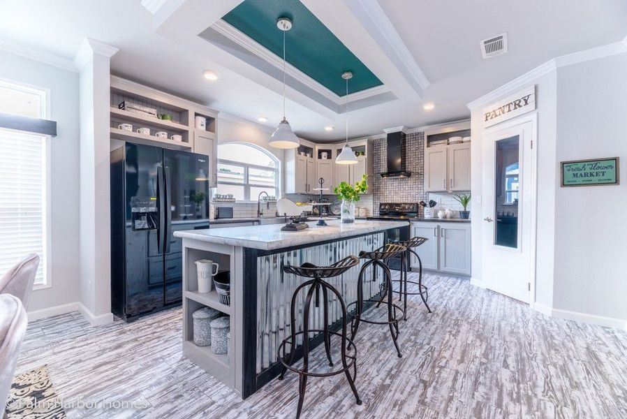 Modern kitchen with island, black appliances, light grey cabinets, and pantry. Turquoise ceiling detail and patterned flooring.