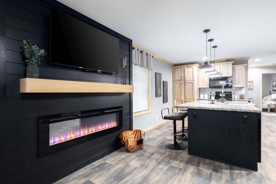 Modern living room with electric fireplace, TV, and kitchen island. Black wall, light wood shelf, gray and beige tones.