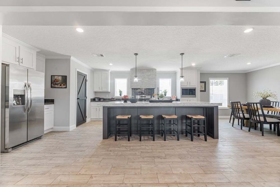 Open-concept kitchen with a large island and dining area. Features stainless steel appliances, black and white accents, and light wood flooring.