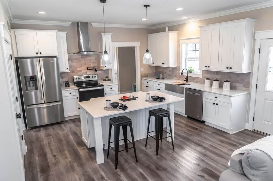 Modern white kitchen with island, stainless steel appliances, and dark floors.