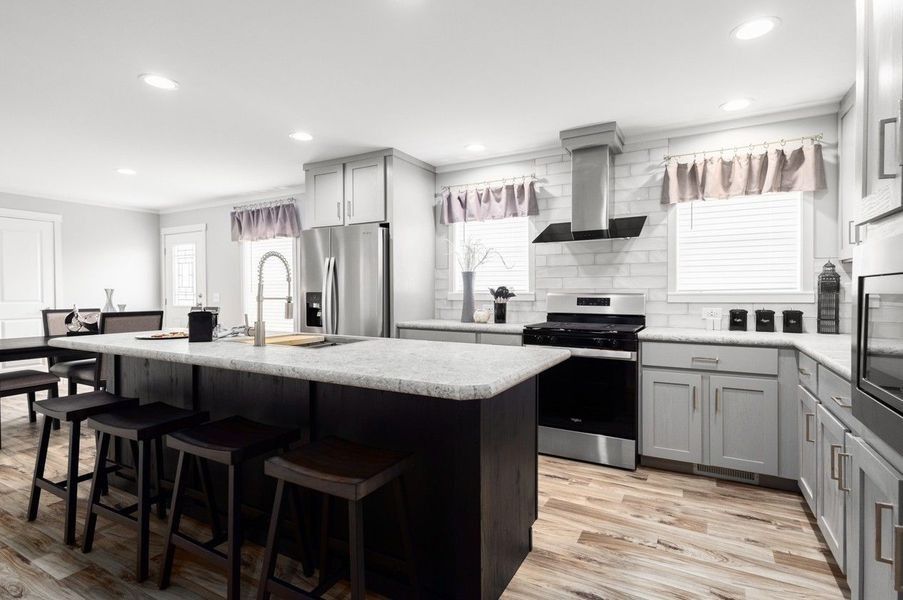 Modern kitchen with island, gray cabinets, stainless steel appliances, and wood-look flooring.