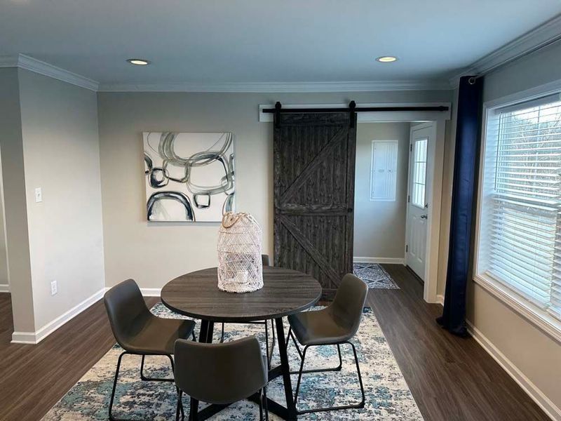 A dining area featuring a round dark table, gray chairs, abstract art, a barn door, and a blue rug.