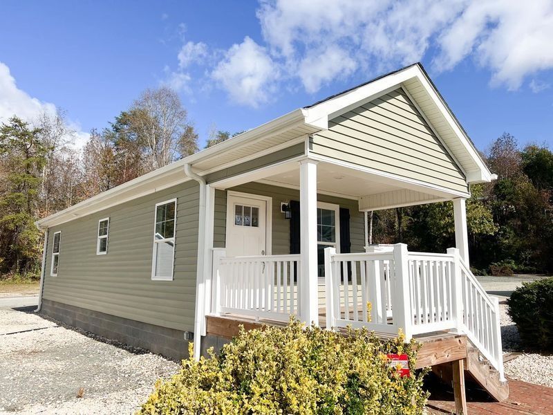 Small, light green house with white porch, steps, and railing on a sunny day.