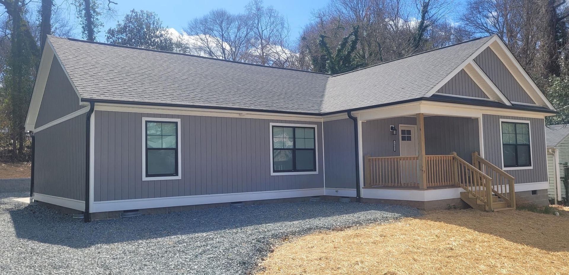 A single-story house with gray siding, a covered porch, and a gravel driveway.