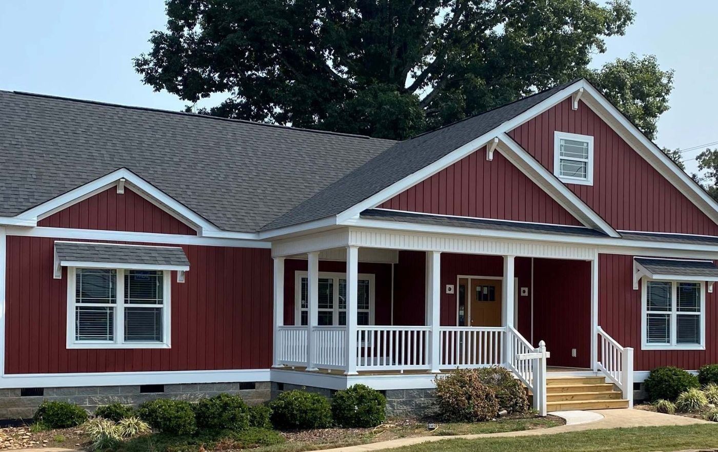 Red house with white trim, porch, and dark gray roof against a sunny sky.