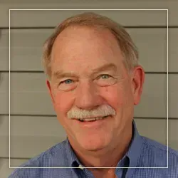 Smiling older man with mustache and blue eyes, in blue shirt, outdoors.