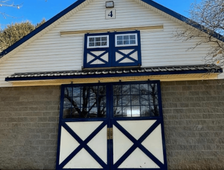 White barn with blue trim and doors. Number 4 above a window. Exterior shot.