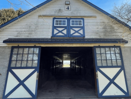 White and blue barn with open doors revealing a long interior aisle, blue sky visible.