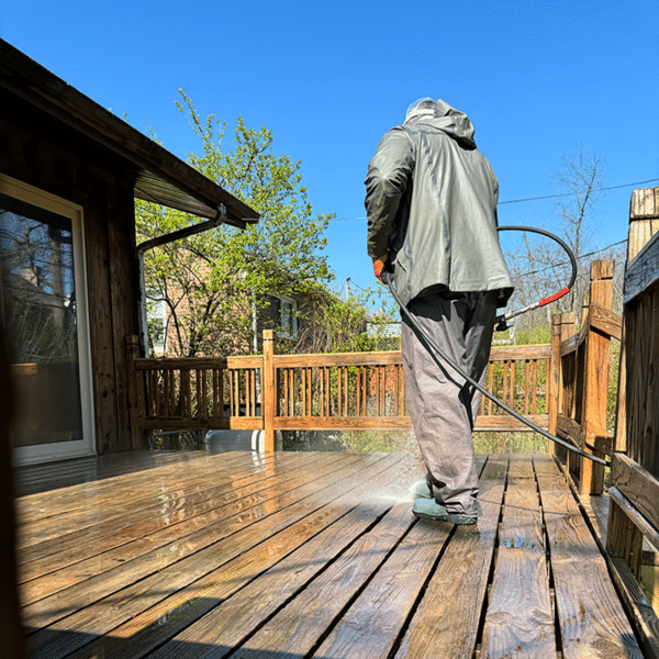 Person pressure washing a wooden deck on a sunny day.